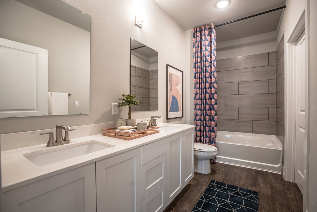 South College Station, TX Apartments - Caprock Crossing - Spacious Bathroom with a Tub with Grey Tile, Double-Sinked Vanity, and Wood-Style Flooring