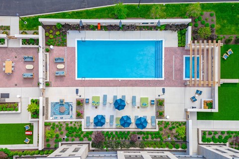 A large swimming pool is surrounded by a white building and blue umbrellas.