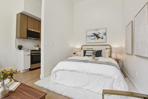 A bedroom with a large bed and a kitchen area in the background.