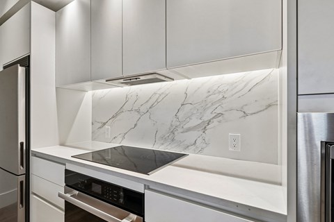 A kitchen with white cabinets and a marble backsplash.