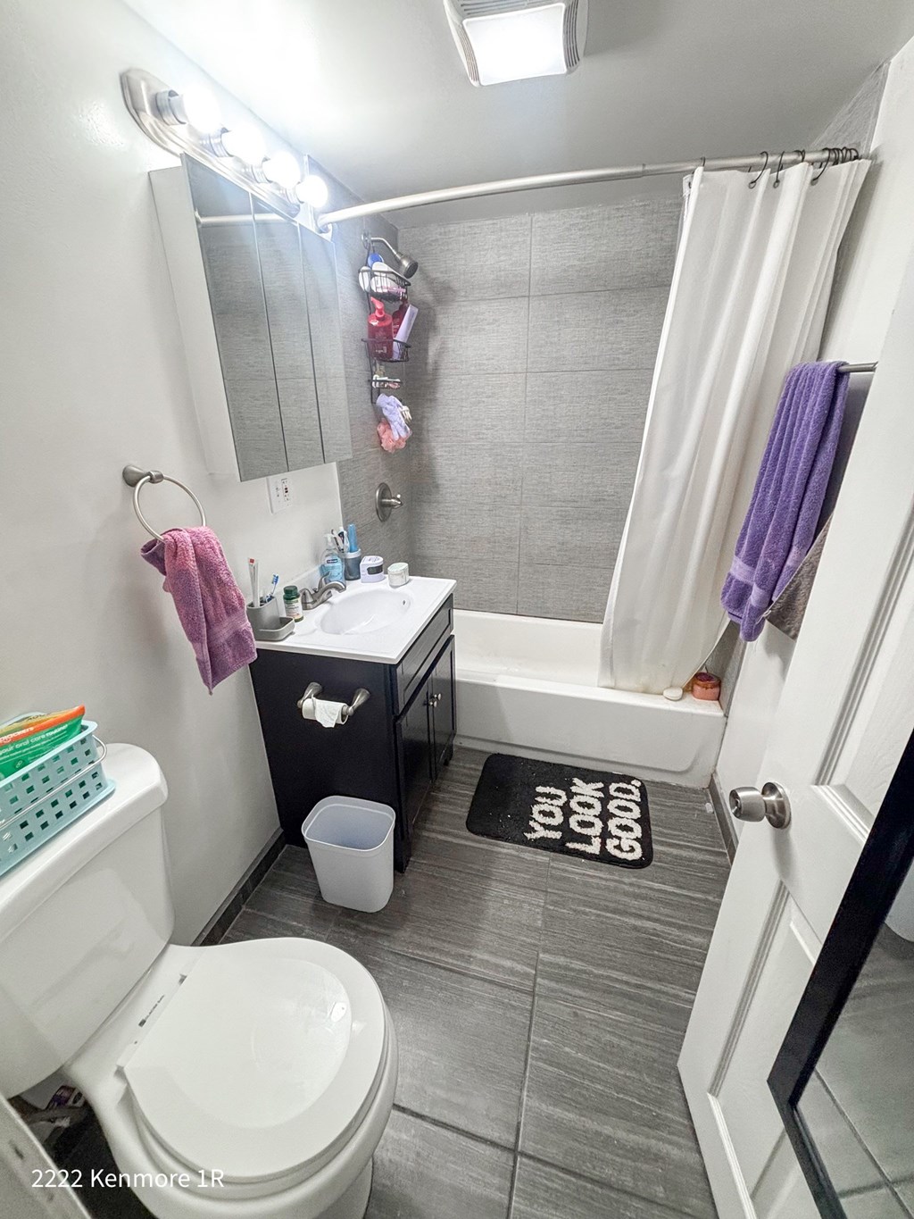 A bathroom with a toilet, sink, and a You Look Good doormat.