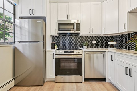 A kitchen with white cabinets and a black and white tiled backsplash.