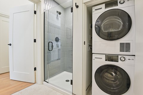 A white door is open to a bathroom with a glass shower stall and a washer and dryer.