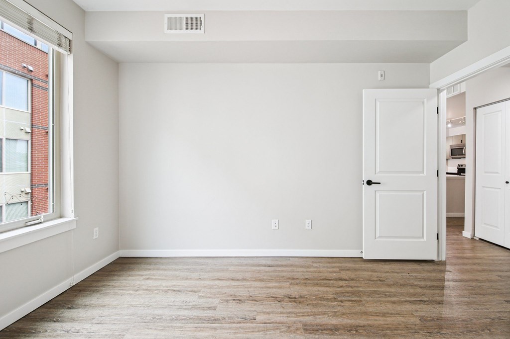 A room with a white door and a window with a brick building outside.