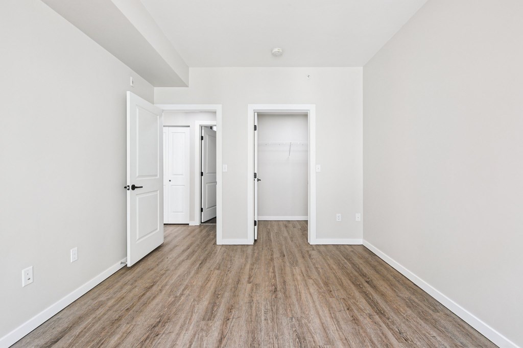 A room with white walls and wood flooring with two doors.