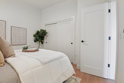 A white bedroom with a bed, pillow, plant, and artwork.