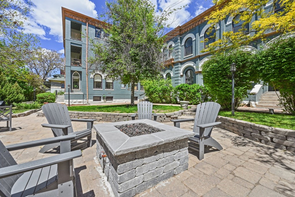 a patio with a fire pit and chairs in front of a building