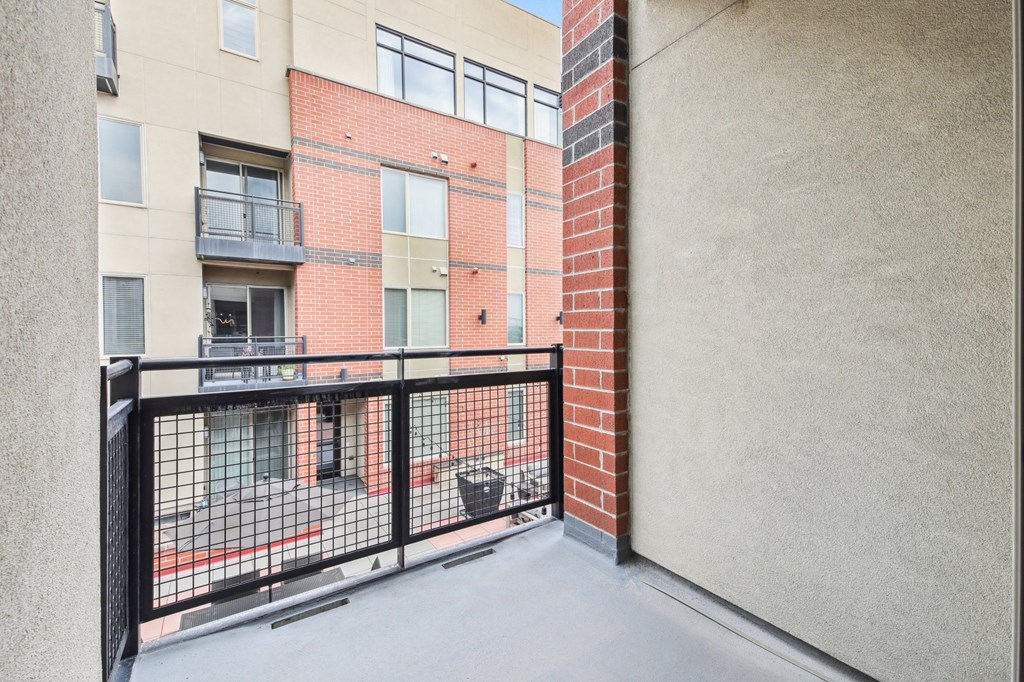 A balcony with a black railing and a brick building in the background.
