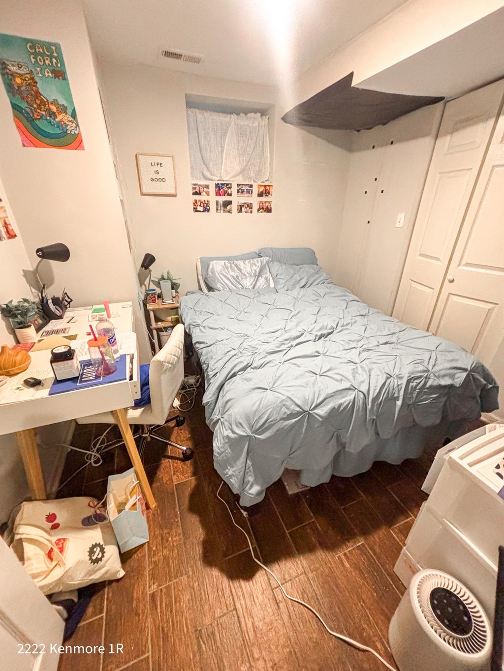 A bedroom with a bed, desk, and fan.