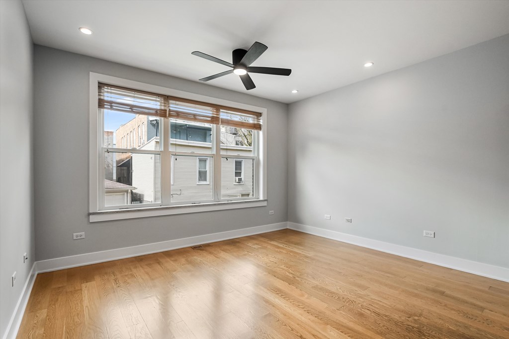 A room with a ceiling fan and a window overlooking a building.