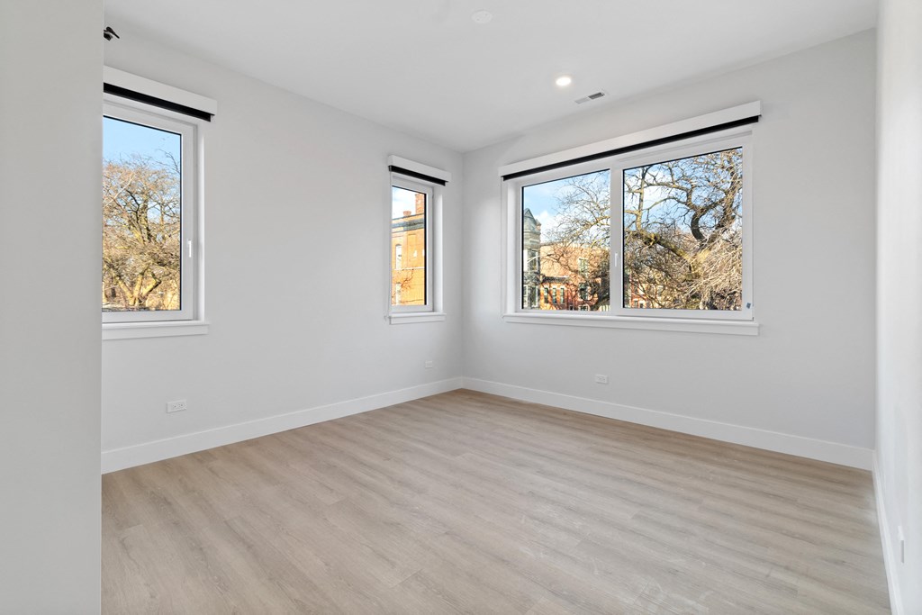 a living room with white walls and wood floors and three windows