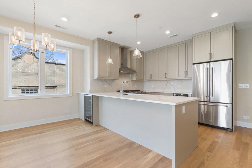 a white kitchen with a large island and a stainless steel refrigerator