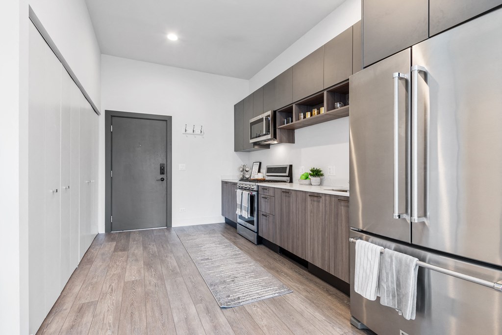A kitchen with white walls and a hardwood floor featuring brand new state-of-art appliances and grey cabinets