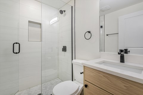 A white toilet is in a bathroom with a white sink and a white shower.