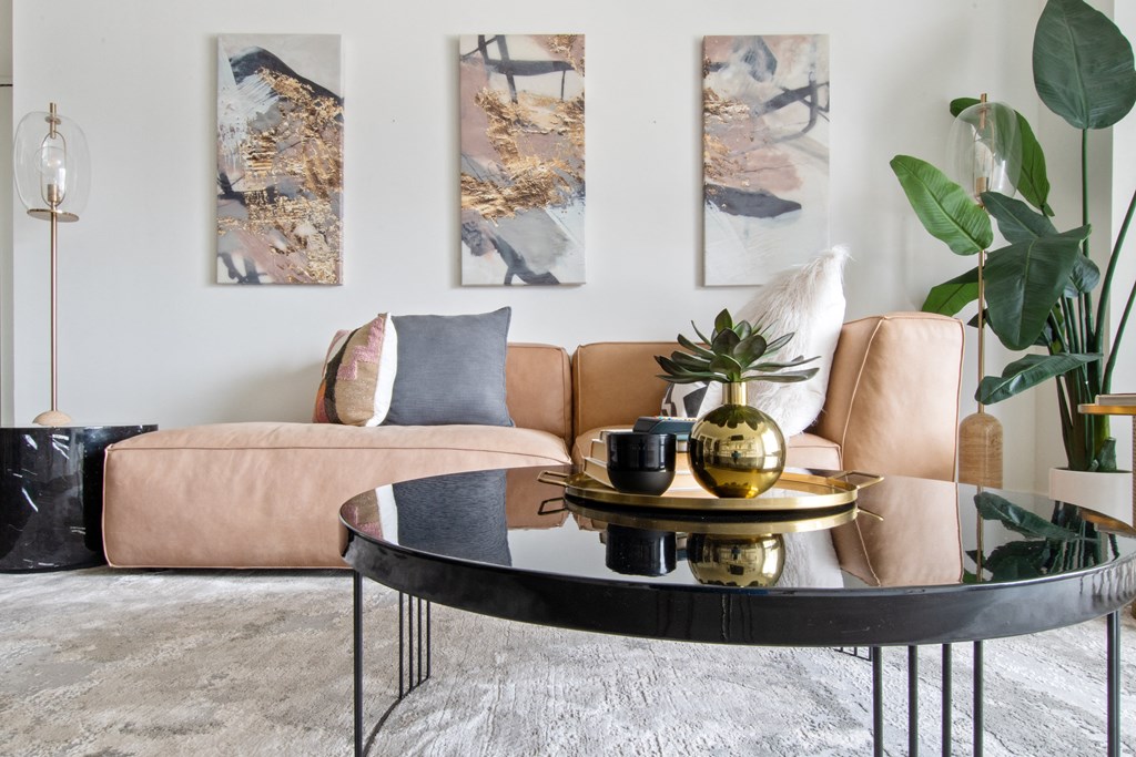 A closeup of living room with a brown couch, round coffee table, and modern paintings on the wall