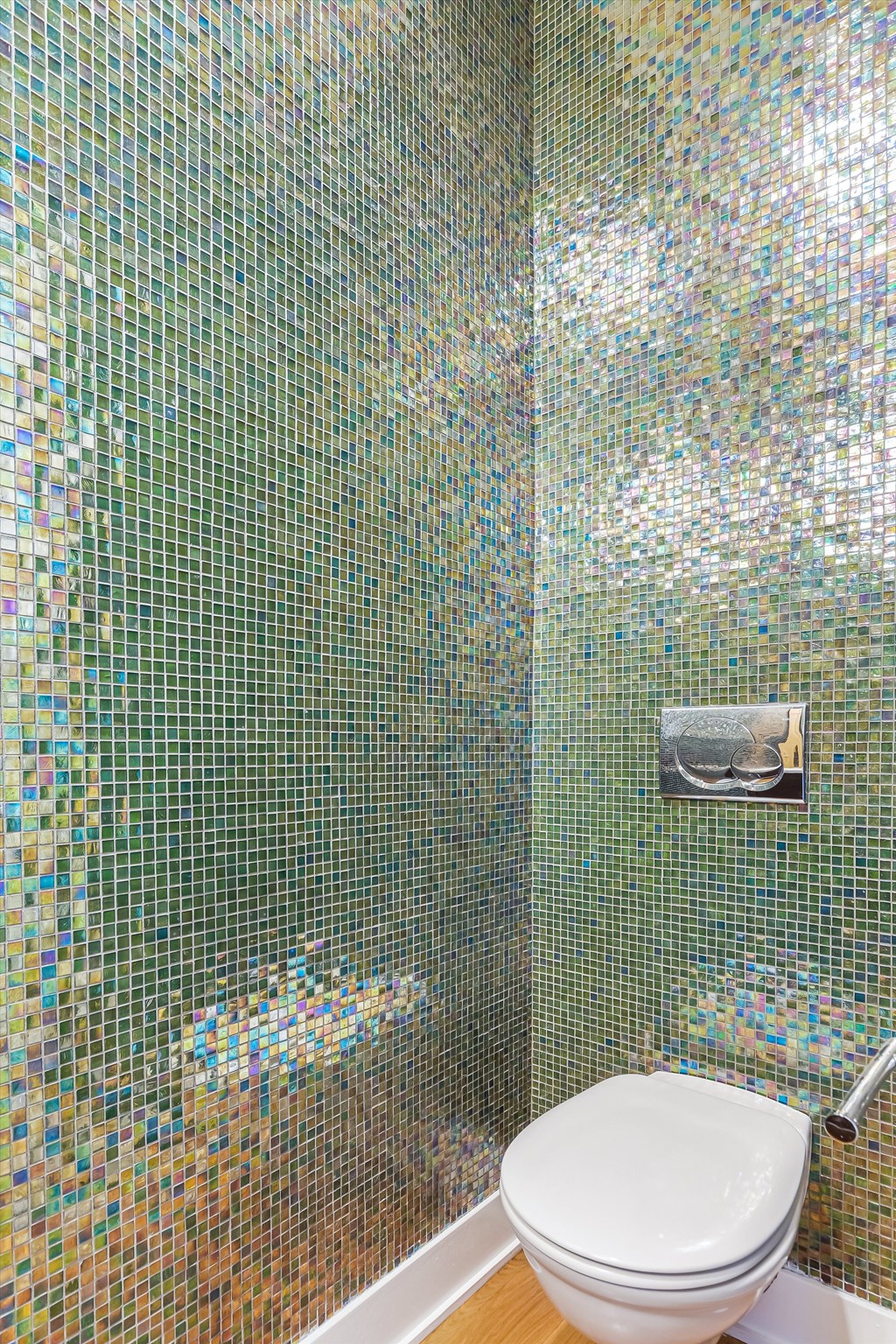 A white toilet in a bathroom with a mosaic tile wall.