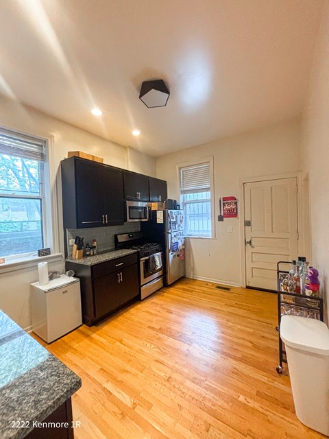 A kitchen with wooden floors and a black fridge.