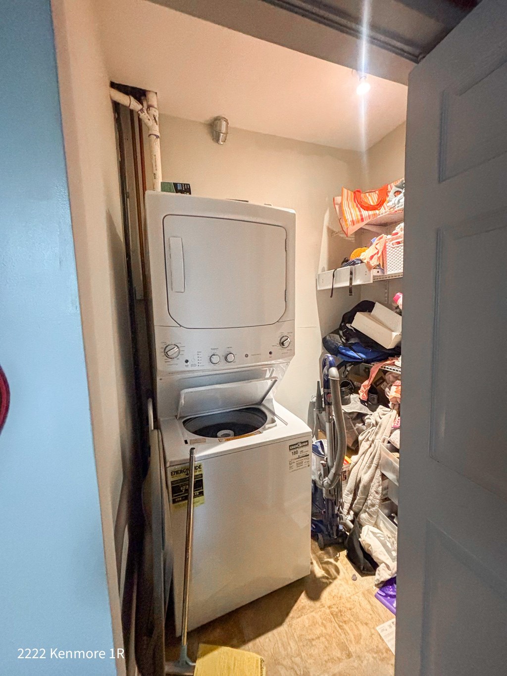 A small white dishwasher is in a narrow space between a wall and a clothes dryer.