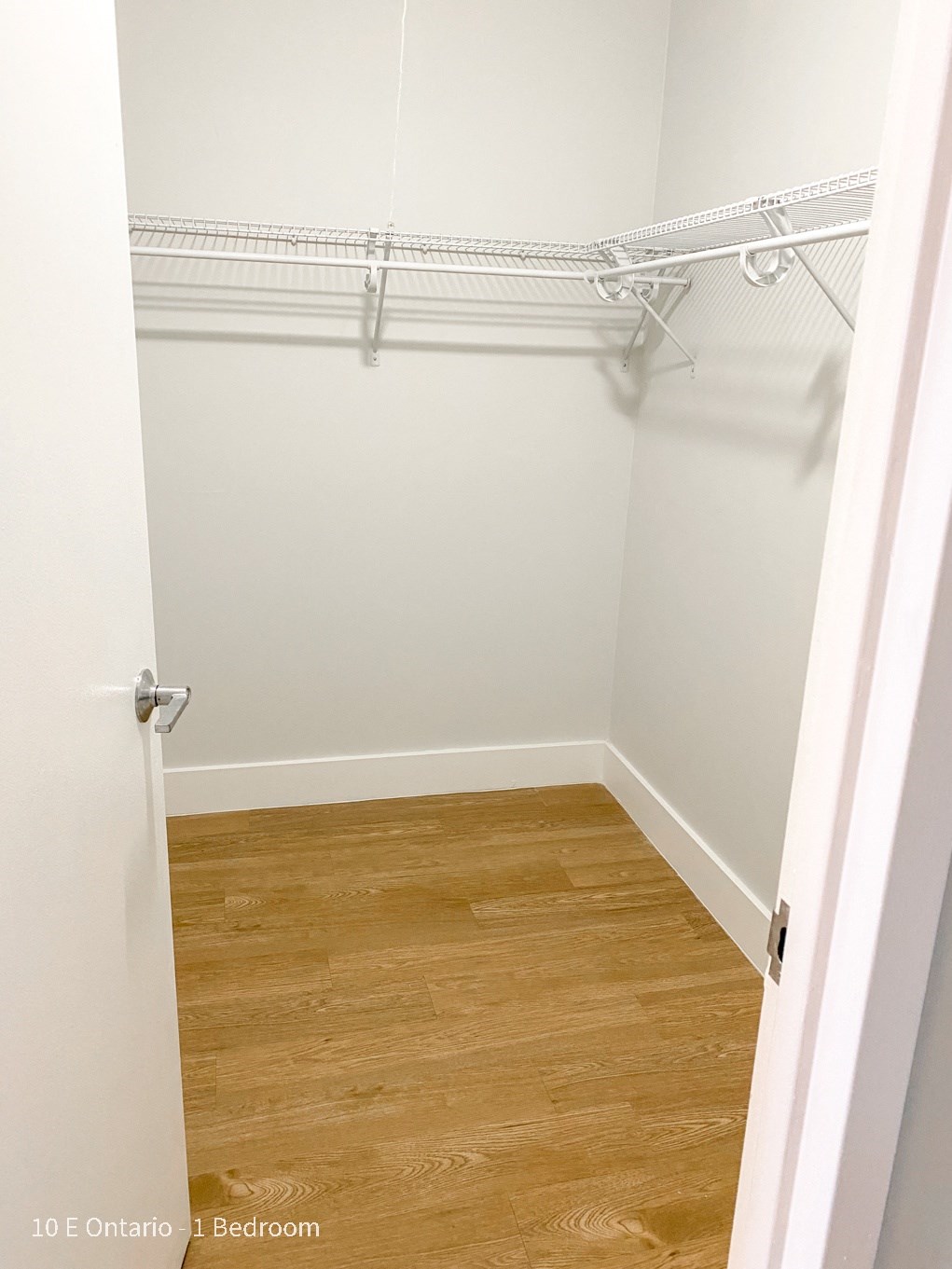 a walk in closet with a wood floor and a white wall with an empty closet