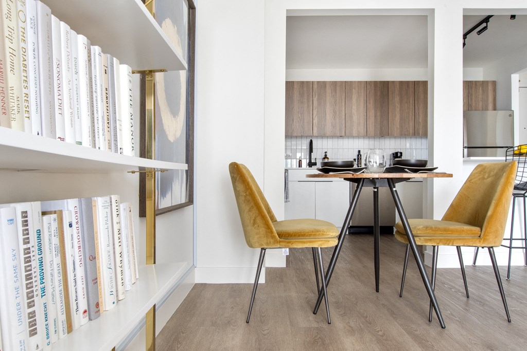 A dining area with a round table and yellow chairs and a kitchen in the background