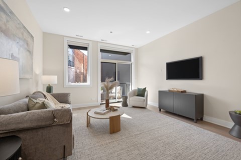 A living room with a grey couch, a coffee table, and a flat screen TV mounted on the wall.