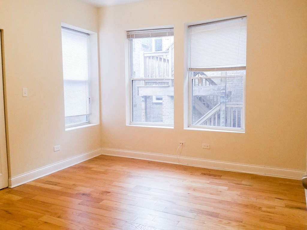 an empty living room with wood floors and three windows
