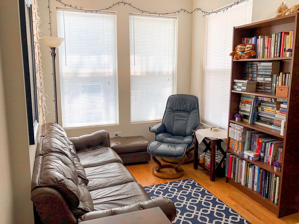 A living room with a brown leather couch, a blue chair, and a bookshelf filled with books.