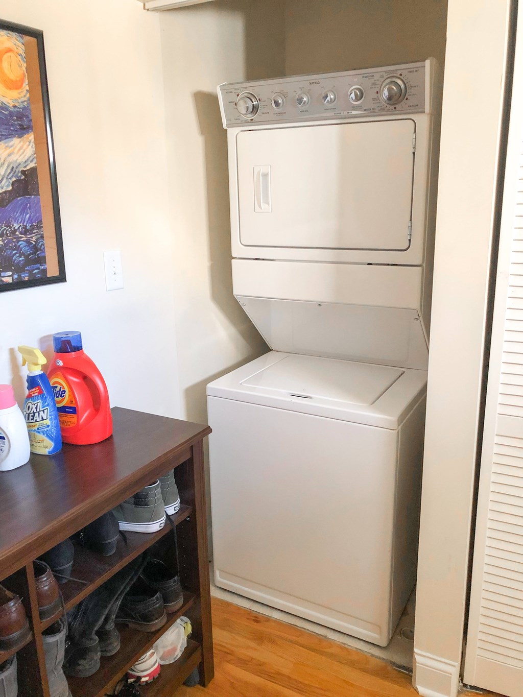 A white dishwasher is in a kitchen next to a wooden shelf with shoes on it.