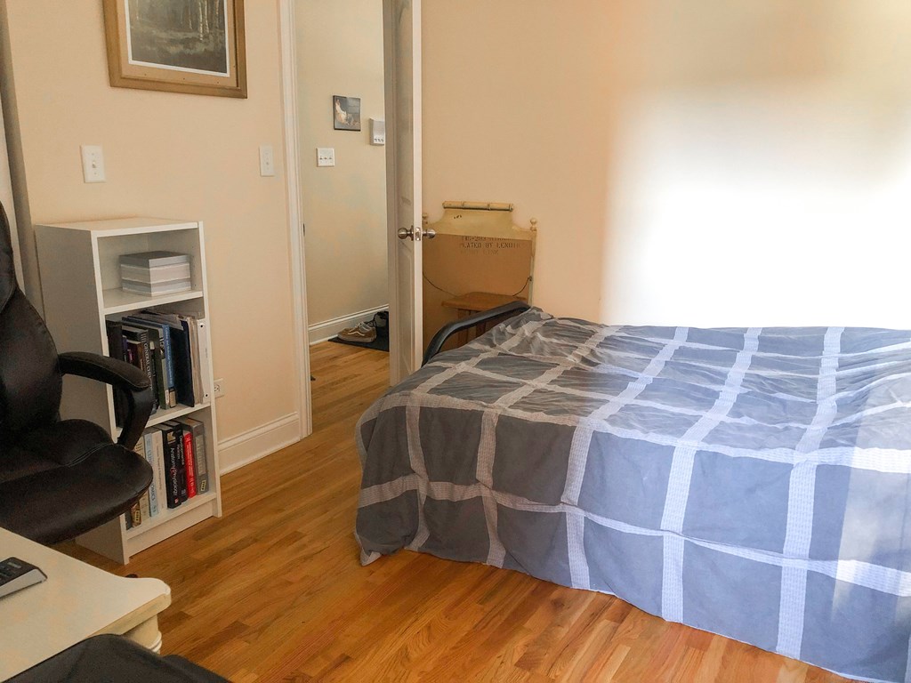 A bedroom with a bed, chair, and a bookshelf.