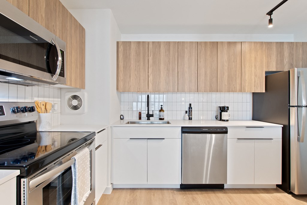 A kitchen with white countertops, wooden cabinets, and brand new stainless steel appliances