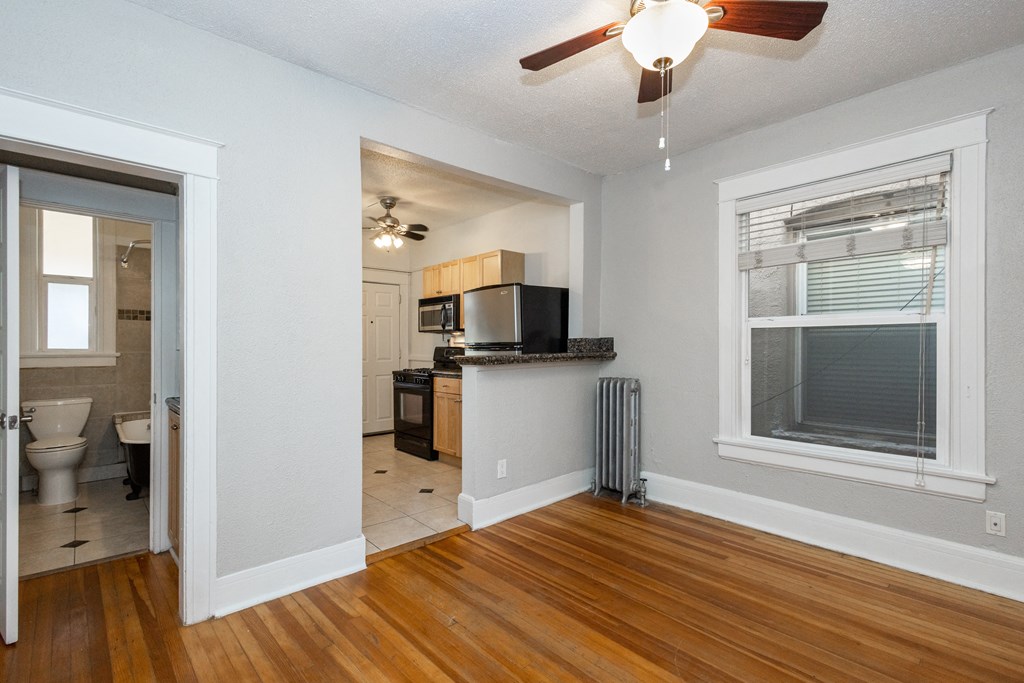 an empty living room with a kitchen and a ceiling fan
