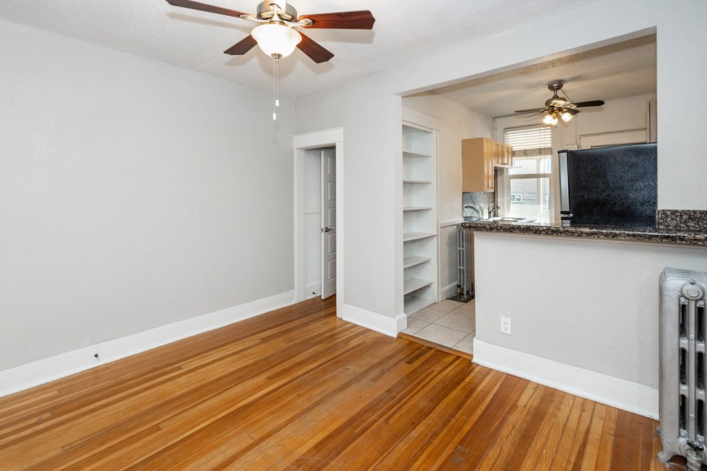 the living room and kitchen of an apartment with wood flooring and a ceiling fan