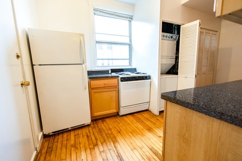 A kitchen with a white fridge and wooden floors.