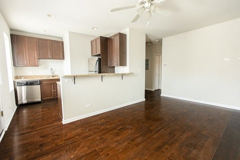 an empty living room with a kitchen and a ceiling fan