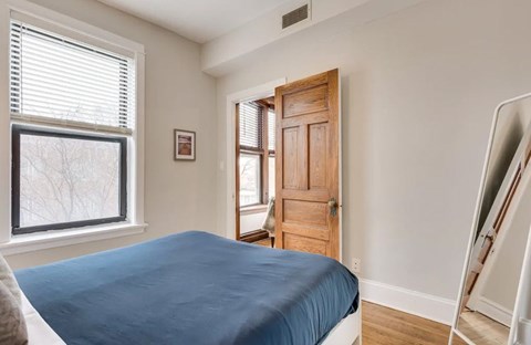 A bedroom with a bed, a window, a door, and a mirror.