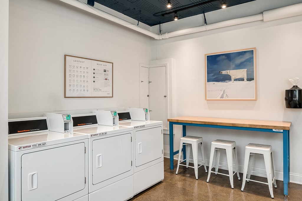 a laundry room with three washing machines and a counter with three stools