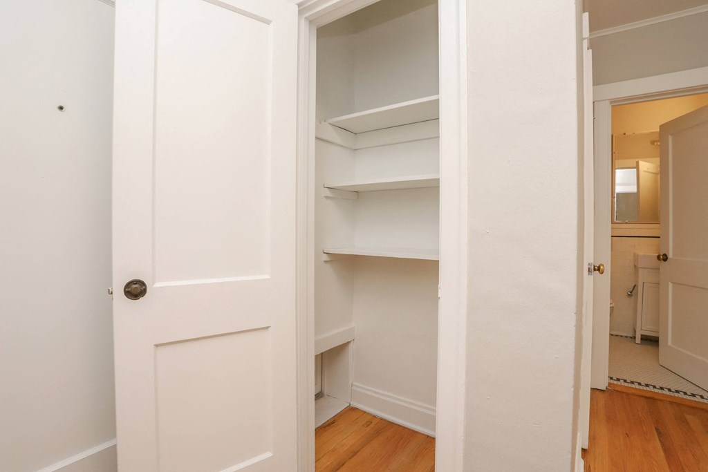 a room with white walls and shelves and a door to a closet
