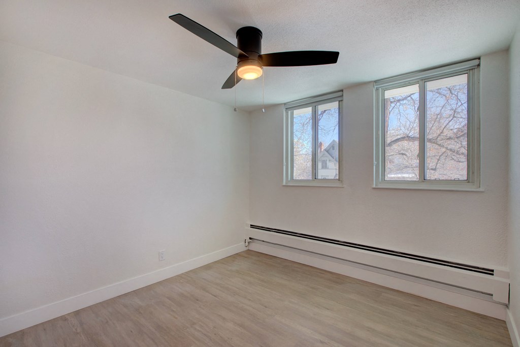 an empty room with a ceiling fan and two windows
