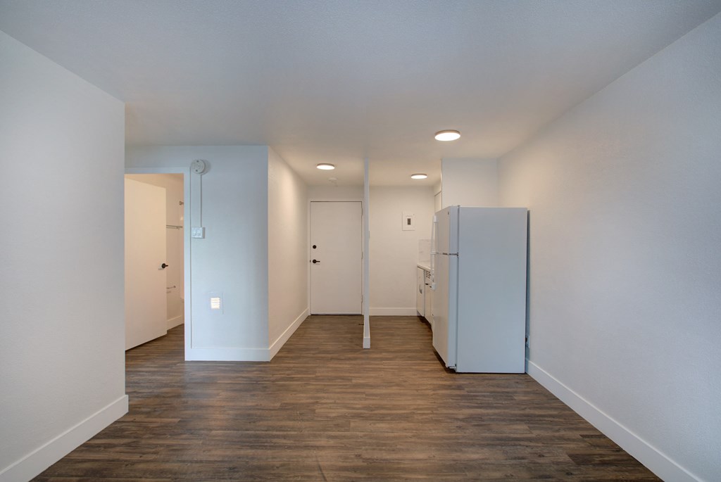 an empty room with a refrigerator and a door into a hallway