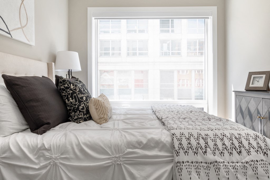 a bedroom with a large window and a bed with white sheets and pillows
