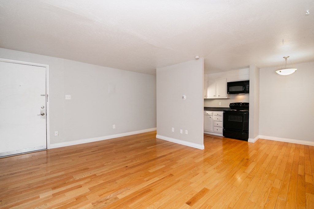 an empty living room with wood floors and a kitchen