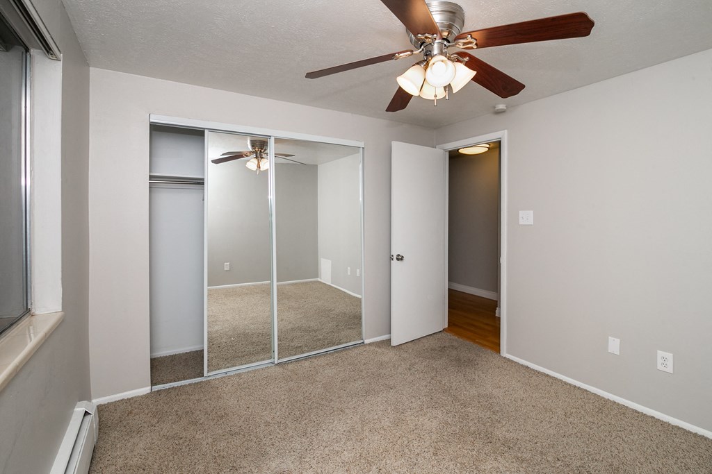 an empty living room with a ceiling fan and mirrored closet