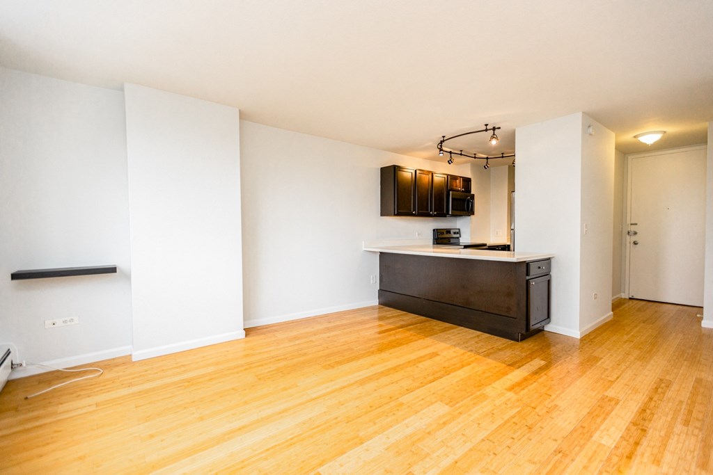 an empty living room and kitchen with wood flooring and white walls