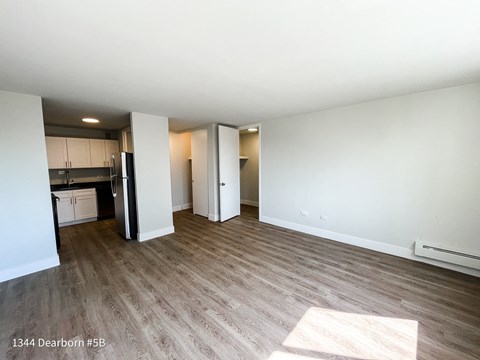 an empty living room with wood flooring and a kitchen