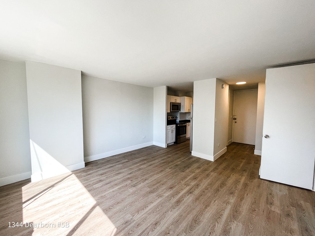 an empty living room with wood flooring and a kitchen