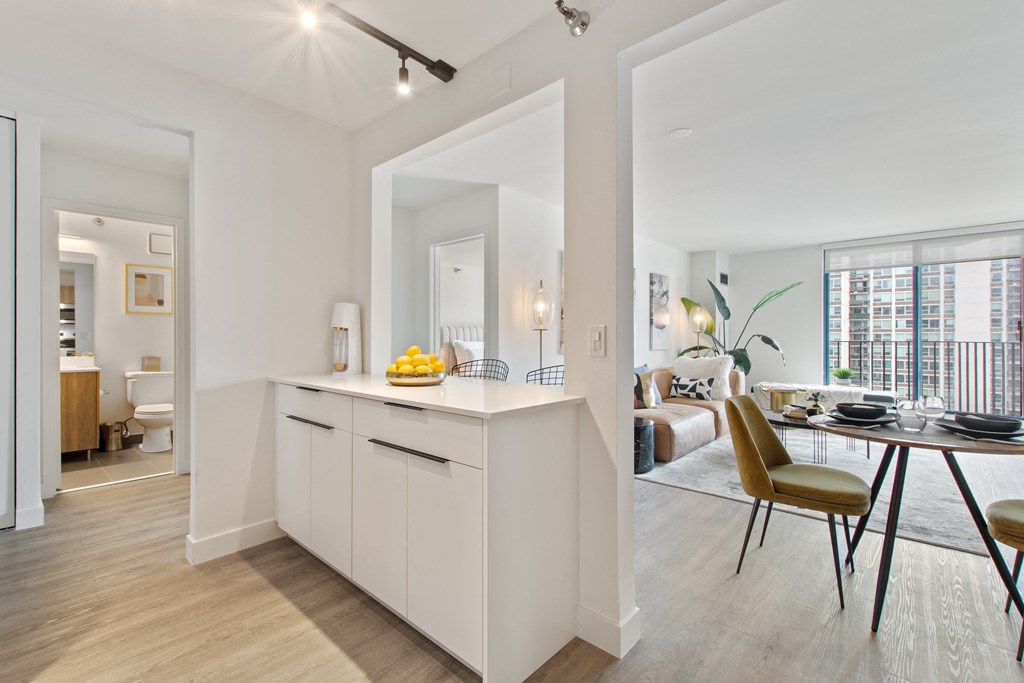 A kitchen with modern white countertops and living room in the backround