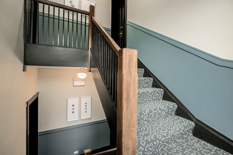 A staircase with a wooden handrail and a light switch on the wall.