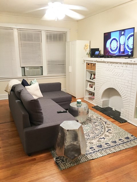 A grey couch with a white pillow and a TV on the wall.