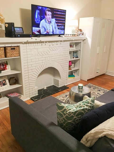 A grey couch with a green pillow is in front of a white fireplace.