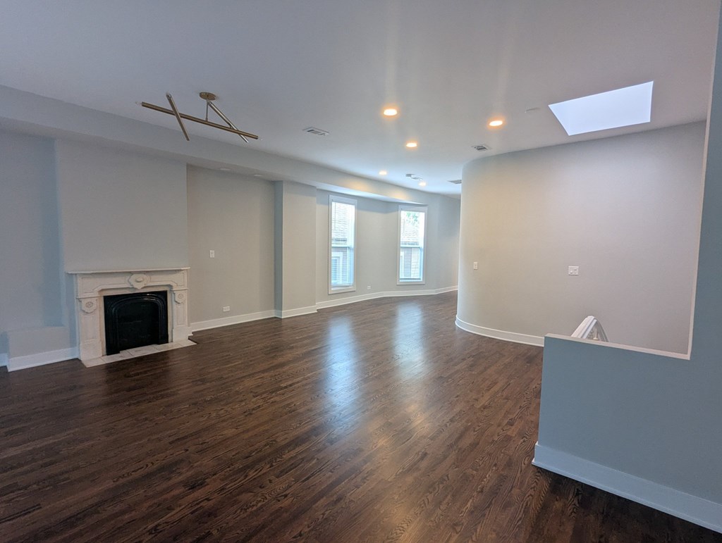 A large empty room with a fireplace and wood flooring.